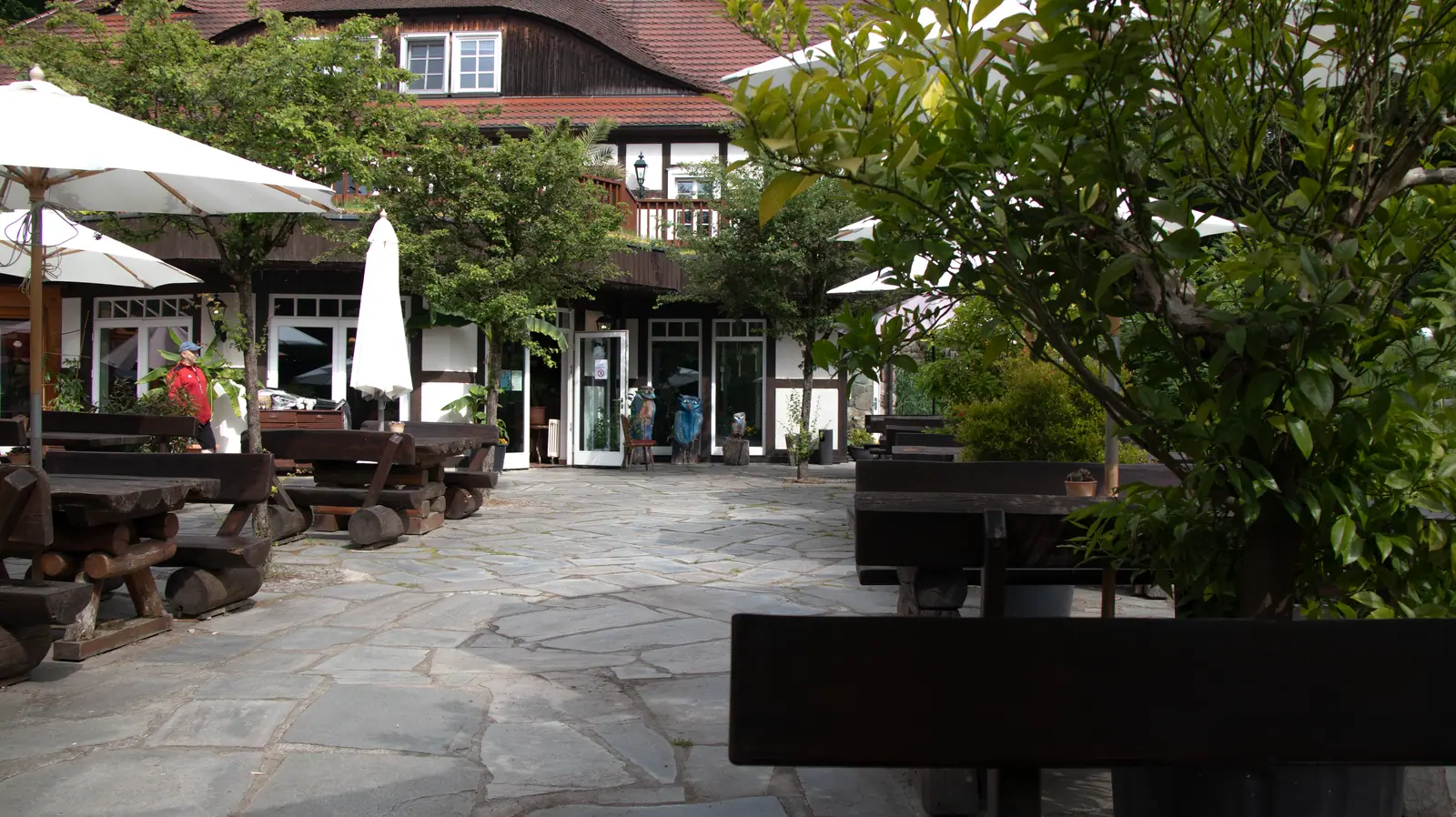 Cortile interno pavimentato della Boltenmühle con rustiche panche di legno, ombrelloni bianchi e l’edificio del ristorante sullo sfondo.